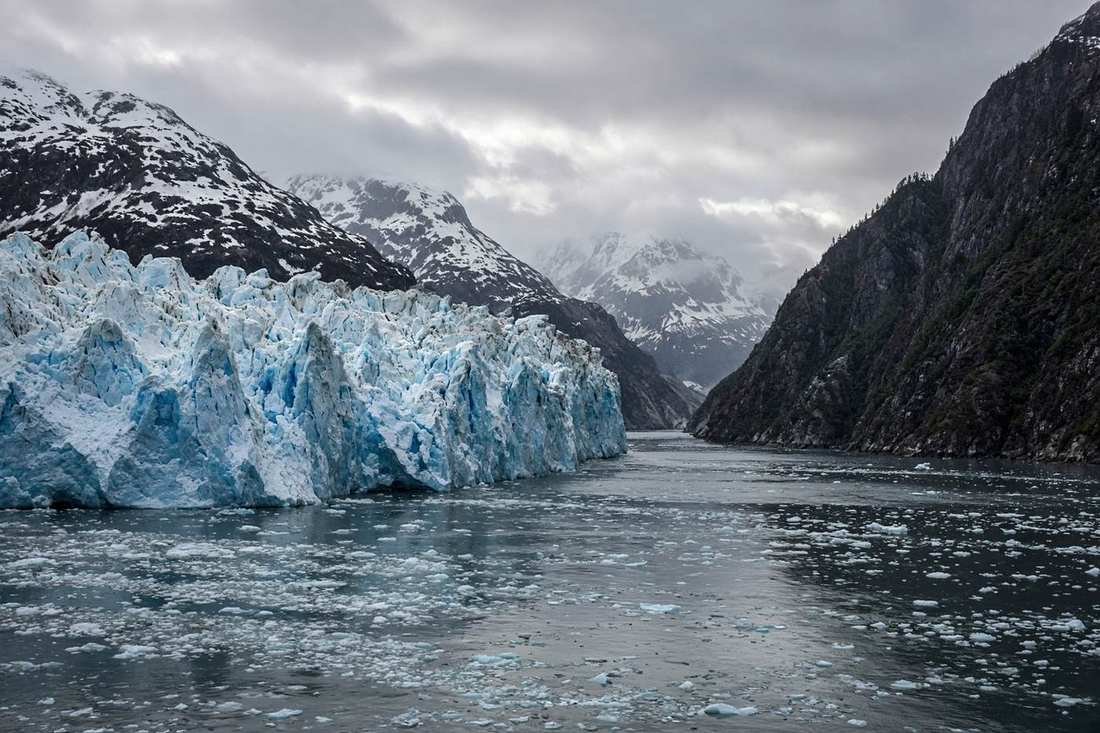 A tidewater glacier meeting dark water in a steep fjord