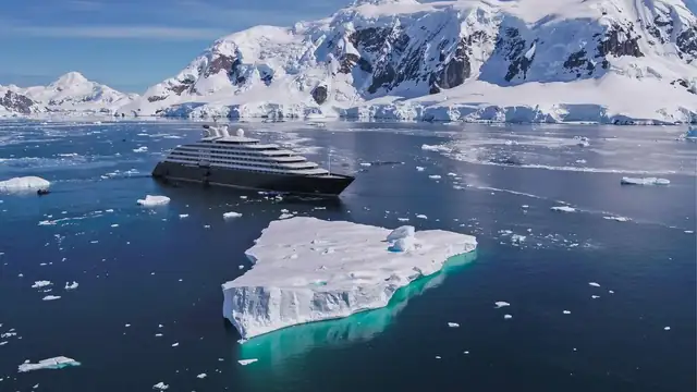 An expedition ship among Antarctic ice, with a turquoise iceberg in front