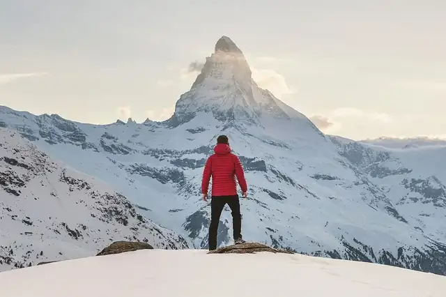 A person in a red jacket facing the Matterhorn across a snowfield