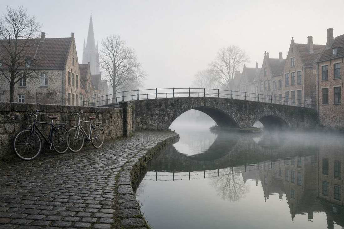 Bicycles beside a misty canal and a stone bridge in an old European town