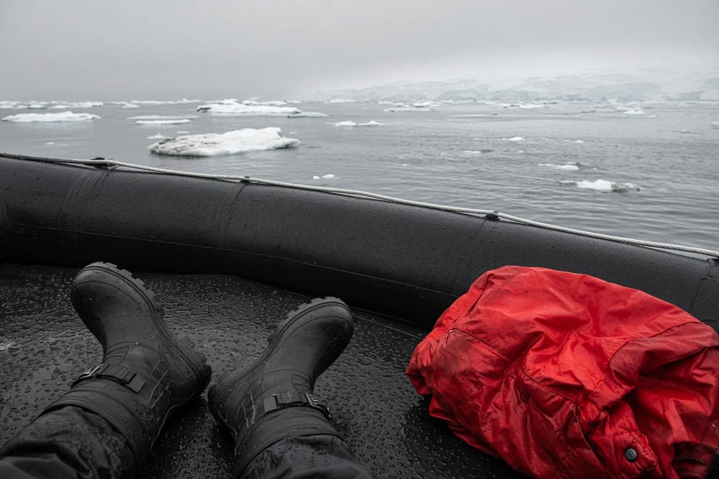 Expedition boots and a red parka on a zodiac, with sea ice beyond