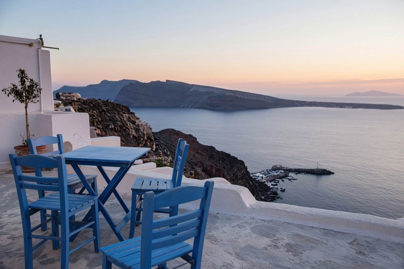 Empty blue chairs on a terrace above a caldera harbor at dawn