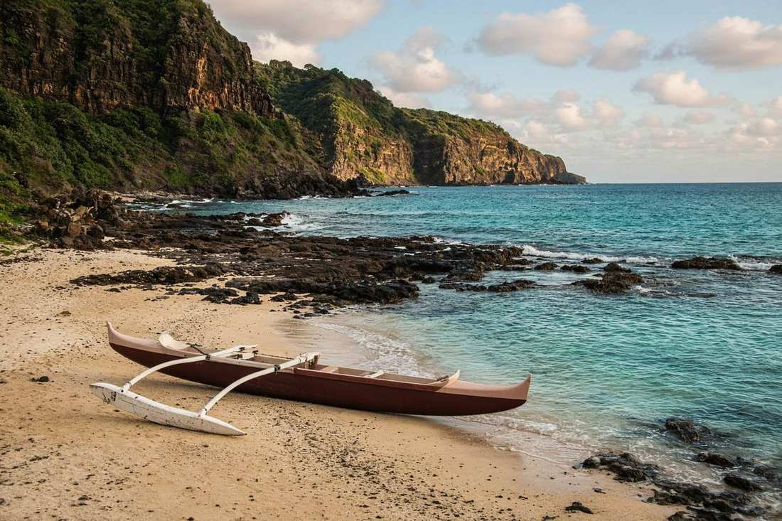 An outrigger canoe on a Hawaiian beach, with cliffs behind it