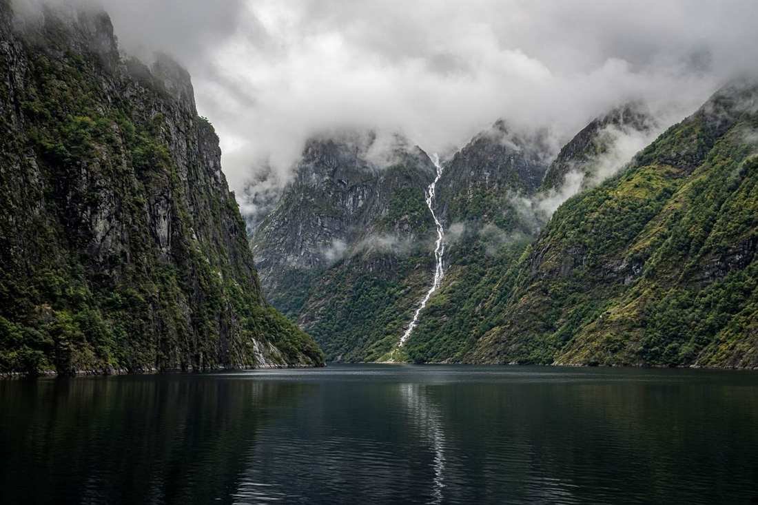 A steep fjord with a thin waterfall and low clouds