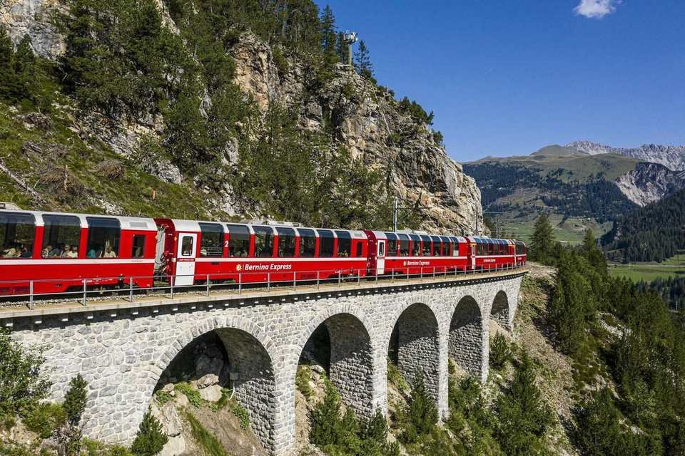 The red Bernina Express on a stone viaduct below a cliff