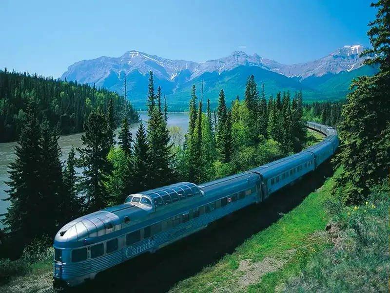 The Canadian, with its dome car, beside a lake and snow-streaked peaks