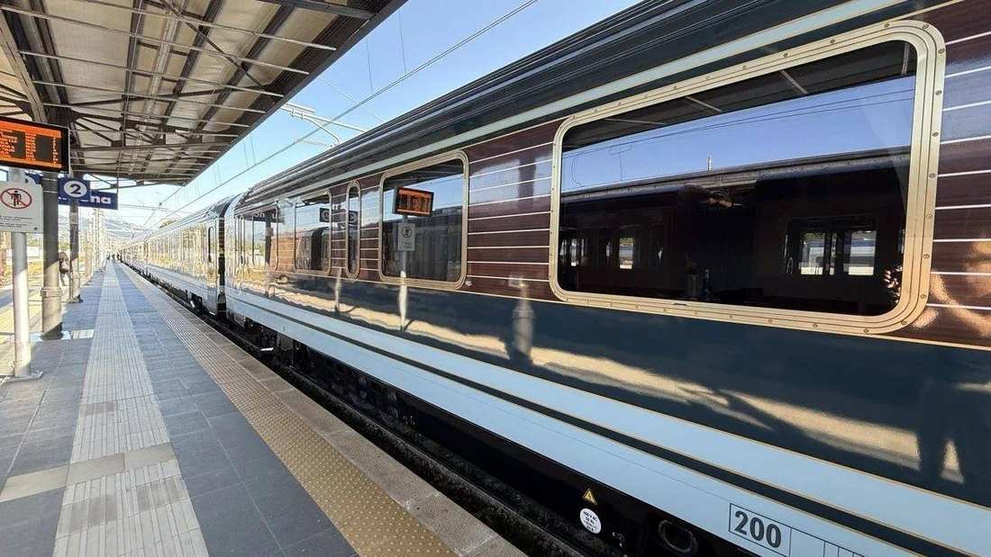 La Dolce Vita Orient Express, a dark blue carriage with brass-framed windows, at a platform