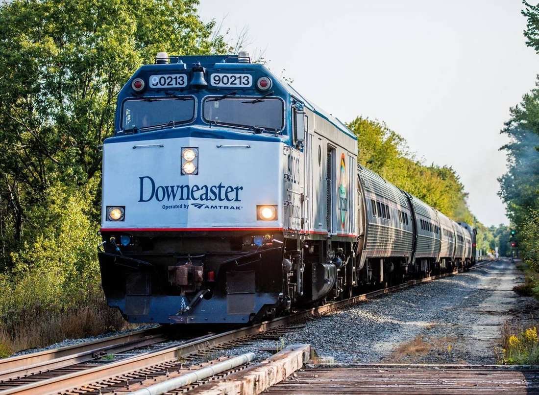 The Downeaster locomotive leading passenger cars through trees