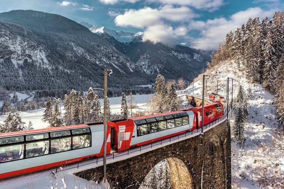 The red and white Glacier Express crossing a stone viaduct in snow