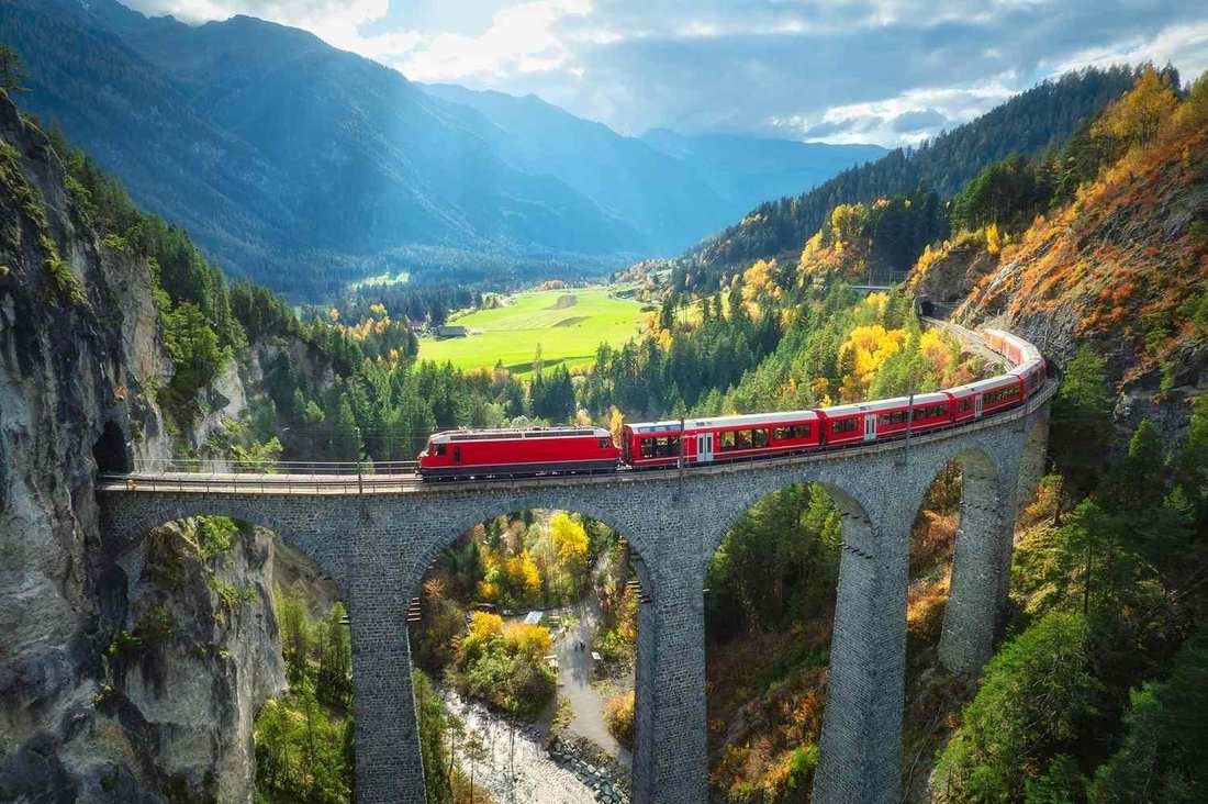 A red train on the Landwasser Viaduct, curving into a tunnel in the cliff