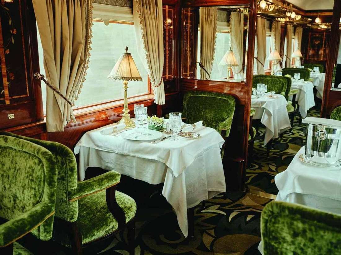 A dining car with white tablecloths, green chairs, and lamps