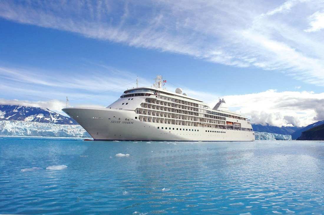 Silver Shadow, a small white Silversea ship, with a glacier behind it