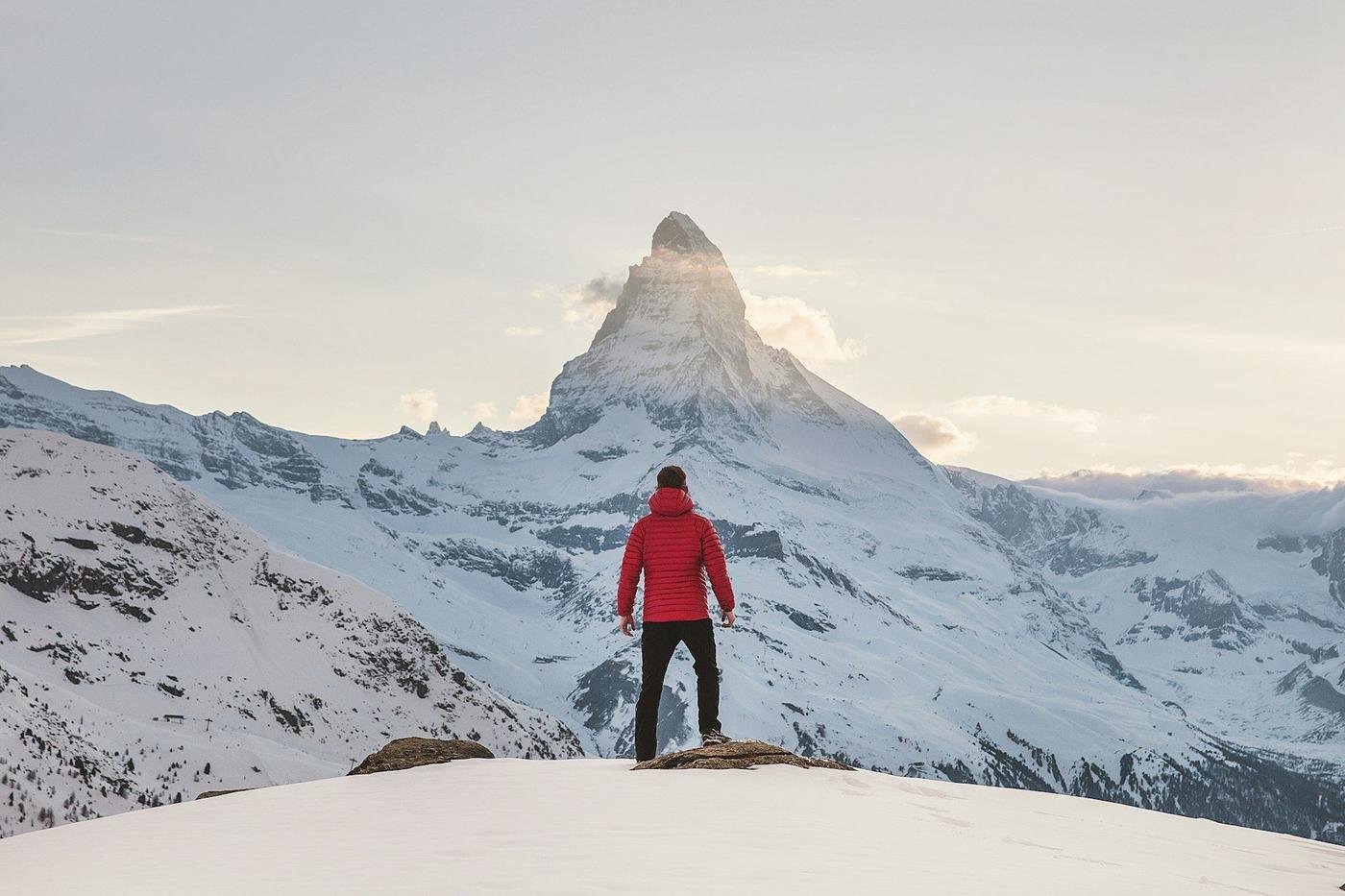 A person in a red jacket facing the Matterhorn across a snowfield