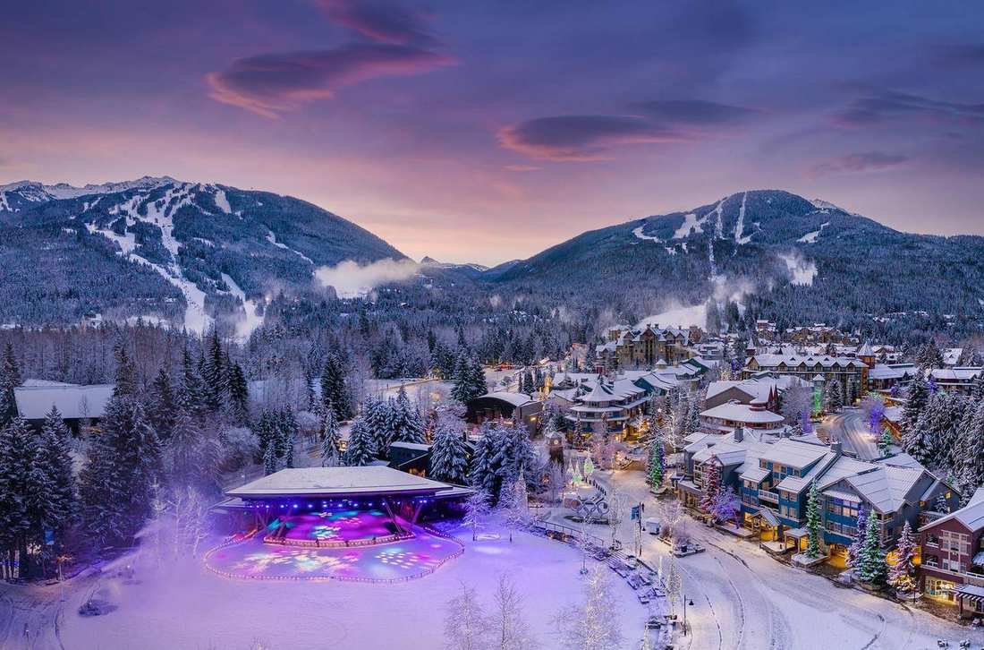 Whistler village at dusk, with ski runs on the mountains behind it